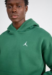 Zelená mikina s kapucňou vyrobená z bavlneného zmesi, s prednou klokankou a bielym logom Jumpman na hrudi. Mäkká textúra a uvoľnený strih.
