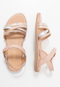 Sandalias rosas y beige con tiras brillantes, acentos metálicos, una plantilla acolchada y un hebilla en el tobillo ajustable. Suela de goma plana.