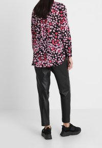 Blusa a maniche lunghe con sfondo nero caratterizzata da un motivo floreale di fiori rosa e rossi, abbinata a pantaloni di pelle neri e sneaker nere.