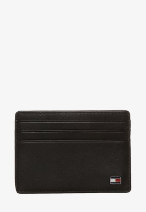 Black leather cardholder featuring four card slots, stitched edges, and a small logo in red and white at the bottom right corner.