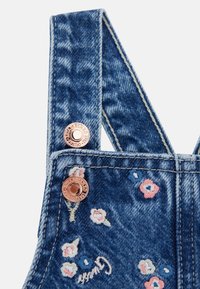 Denim overalls with adjustable straps, featuring floral embroidery in pink and blue, and rose gold hardware buttons. Classic blue wash.