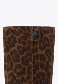 Bruine suède enkelboot met luipaardprint, voorzien van een zwarte decoratieve hardware-accent aan de bovenkant en een gladde, fluweelachtige textuur.