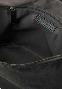 Intérieur d'un sac en tissu noir avec une texture lisse, comprenant une poche zippée sur le côté et une étiquette en cuir portant le logo "TOM TAILOR".