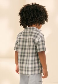 Chemise à manches courtes à carreaux noir et blanc, avec col rabattu et ourlet droit, portée par un enfant, vue de dos.