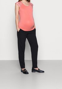 Těhotenský top v korálové barvě s krajkovými rukávy, kombinovaný s černými kalhotami a černými mokasiny. Hladký materiál, přiléhavý střih a pohodlné nošení.