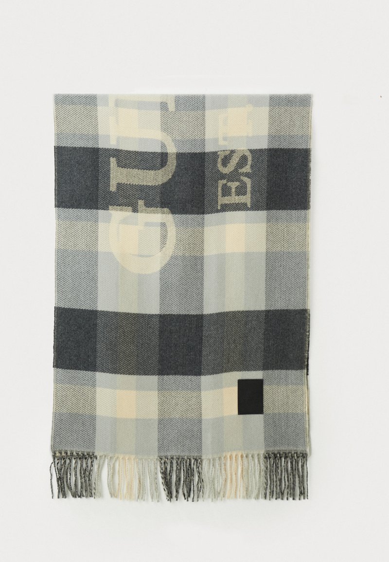 Grå og beige ternet tørklæde lavet af blødt stof, med en sort firkantet accent og frynser i kanterne. Bemærkelsesværdig tekstdesign i kontrastfarver.