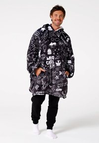 Juodas pūkuotas perdidintas džemperis su baltais grafiniais raštais. Su gaubtu, ilgomis rankovėmis ir kišene. Dėvimas su juodomis kelnėmis ir baltais kojinėmis.