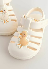 Cream-colored children's sandals with duck-shaped decorations on the top, featuring open straps and a hook-and-loop ankle closure.