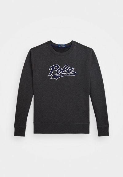 Tumši pelēks krekls ar apaļu izgriezumu, garām piedurknēm un ribotām aprocēm. Uz priekšpuses ir izteikts izšuvums ar "Polo Ralph Lauren" logotipu.