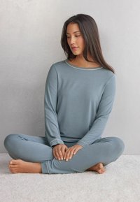 Ljusblå långärmad pyjamasset med rundad halsringning och vit kant, tillverkad av mjukt tyg, med tajta byxor och en avslappnad passform.