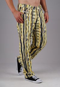 Loose-fitting pants with a yellow, black, and white abstract pattern. Features two front pockets and a comfortable waistband. Paired with black sneakers.