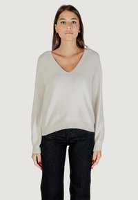 Pull V en gris clair avec des manches longues, présentant un léger éclat et un ourlet côtelé, associé à un jean en denim foncé.