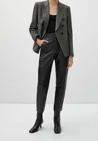 Blazer grigio doppiopetto, top nero, pantaloni in pelle nera e stivaletti neri alla caviglia, con texture lisce e vestibilità su misura.