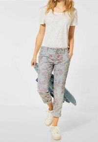 Blommönstrade byxor i ljusblått med uppvikta fållar, tillsammans med en vit kortärmad skjorta och vita sneakers. Jeanjacka slängd över armen.