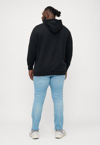 Sudadera con capucha negra de manga larga, combinada con jeans azul claro y zapatillas grises, vista desde atrás.