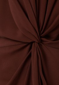Tessuto marrone con una superficie morbida e texturizzata, caratterizzato da dettagli drappeggiati che creano un effetto torcigliato al centro.