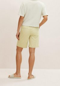 Des shorts jaune clair avec une texture lisse et un ourlet retourné, associés à un haut blanc court et des sandales à enfiler gris clair.