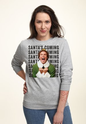 Un sweat-shirt gris avec un motif représentant un personnage aux cheveux bouclés portant une tenue verte et un col blanc, avec un texte noir répétant "SANTA ARRIVE".