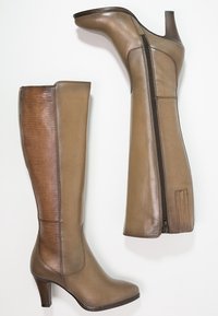 Botas de cuero marrones, hasta la rodilla, con tacón alto, detalles texturizados en el eje y un cierre lateral para ponerlas y quitarlas con facilidad.