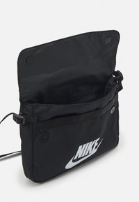 Melnas neilona somas ar priekšējo kabatu, kurā ir liels balts Nike logo. Tām ir pogu aizdare un siksna ar tīkla pievilkumu, lai ērti valkātu.