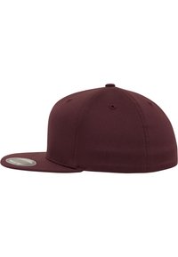 Burgundy snapback cap with a flat visor, made of smooth fabric, featuring ventilation holes and a circular logo patch on the side.