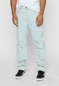 Jeans din denim albastru deschis, cu croială dreaptă, având un design clasic cu cinci buzunare și purtați cu adidași negri.