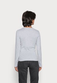 Harmaa pitkähihaisessa paidassa on pyöreä kaula-aukko ja se on valmistettu pehmeästä kankaasta. Takana näkyy istuva muotoilu ja yksinkertainen rakenne. Yhdistetty mustiin farkkuihin.