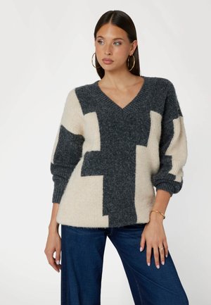 V-Ausschnitt Strickpullover in Dunkelgrau und Creme, mit einem abstrakten Blockmuster. Lange Ärmel mit gerippten Bündchen, weiche Textur.