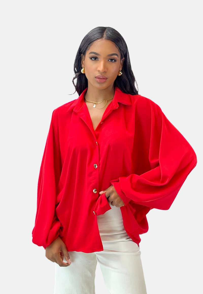 Red, long-sleeve button-up shirt made of smooth fabric, featuring a relaxed fit, a collar, and oversized sleeves. Gold buttons detail the front.