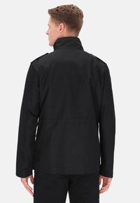 Sort jakke med høj krave, enkelte skulderepauletter, glat tekstur og lige snit, set bagfra.