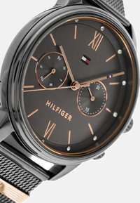 Montre en acier inoxydable noir avec un cadran gris foncé texturé. Comprend des accents en or rose, des chiffres romains, deux sous-dials et un bracelet en maille.