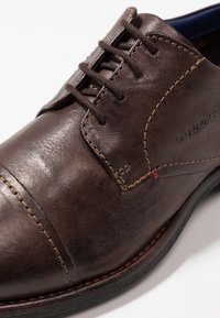 Chaussure habillée marron en cuir à lacets avec coutures détaillées et logo "bugatti" embossé sur le côté.