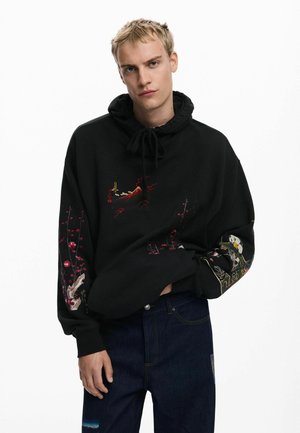 Sort hættetrøje med broderede designs af et bjerg og kirsebærblomster på forsiden samt farverige mønstre på ærmerne. Blødt stof, løs pasform.