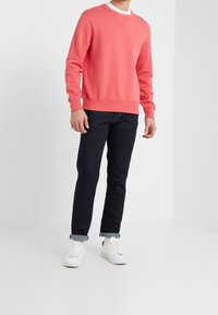 Koraal sweatshirt, ronde hals, gemaakt van een katoenmix, gecombineerd met donkerdenim jeans en witte sneakers, met omgeslagen mouwen.
