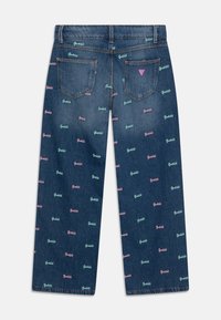 Denim jeans med et mønster af "Guess" logoer i pink, grøn og blå. Lige ben, to baglomme og et trekantet logo ved taljen.