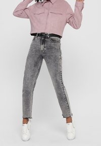 Avskuren dammrosa skjorta med två bröstfickor, kombinerad med högmidjade grå jeans med fransade fållar och en avsmalnande silhuett. Vita sneakers.