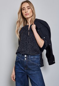 Hemd mit Marine-Muster und weißen geometrischen Designs, mit Knopfleiste, kombiniert mit taillierten dunkelblauen Jeans, die über zwei Knöpfe und dezente Nähte verfügen.
