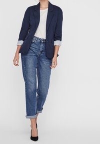 Mörkblå blazer med upprullade ärmar, i kombination med en ljus t-shirt och raka blå jeans. Svarta klackar fulländar looken.