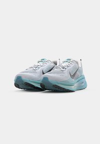 Bežecké tenisky Nike so šedou a bielou sieťovinou, tyrkysovými akcentmi, polstrovanou podrážkou a čiernou gumovou podrážkou pre lepšiu priľnavosť.