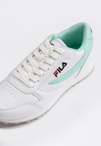 Baskets blanches avec des accents vert menthe, surface en cuir texturé, bout rond et fermeture à lacets. Présente un logo prominent sur le côté.