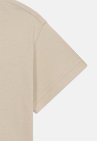 Lys beige t-shirt detalje med en nærbillede af ærmet. Har en glat bomuldsstruktur og kort, opsmøgget ærmedesign med pæne stikninger.