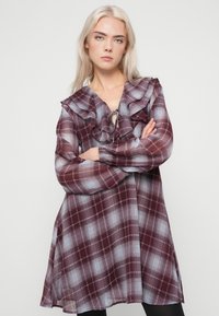 Κόκκινο και μπλε καρώ φόρεμα με λαιμόκοψη με βολάν, μακριά μανίκια και χαλαρή εφαρμογή. Το ύφασμα φαίνεται ελαφρύ και ελαφρώς διακριτικό.