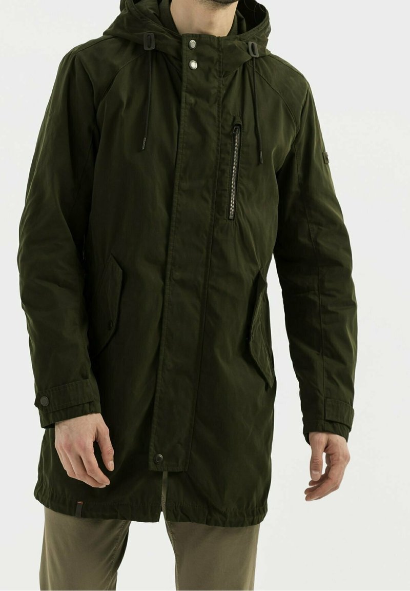 Chaqueta larga verde oliva con capucha, cierres de cremallera y botones a presión, bolsillos laterales y cuerdas ajustables. Hecha de una tela texturizada.