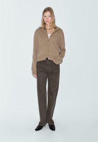 Brun knappad cardigan i mjukt tyg, i kombination med mörkbruna vida byxor. Utseendet fulländas med svarta skor. Enkel och avslappnad design.