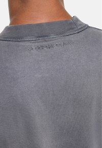 Szary sweatshirt z okrągłym dekoltem, wyposażony w ściągacz i haftowany napis "GOODFORNOTHING" na plecach. Gładka bawełniana faktura.