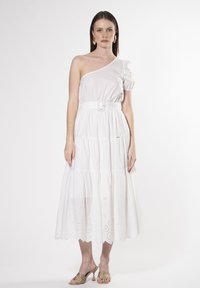 Vestido blanco de un solo hombro con manga abullonada, cinturón en la cintura y falda de volantes. Presenta un detalle de broderie anglaise en el dobladillo. Textura de tela suave.