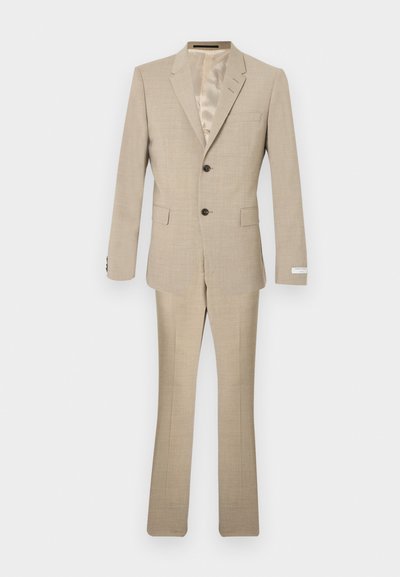 Μπεζ κοστούμι κατασκευασμένο από υφασμάτινη υφή, με σακάκι δύο κουμπιών, πέτο με εγκοπές και παντελόνια ραμμένα με ελαφριά φουσκώματα.