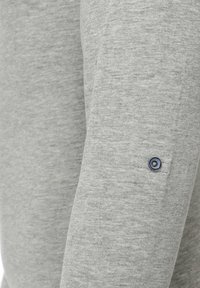 Graues Langarmshirt aus weichem Stoff, mit einem sichtbaren Knopfdetail am Ärmel und blauen sowie silbernen Akzenten.