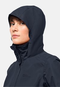 Veste imperméable bleu marine avec une capuche ajustée et un col haut. Équipée d'un logo sur la poitrine gauche et d'une texture lisse et mate.