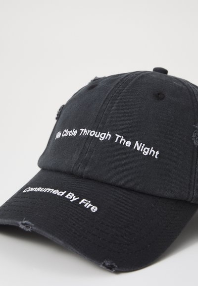 Casquette en coton noir avec un texte brodé blanc : "Nous traversons la nuit" et "Consommé par le feu". Détails usés sur la visière.